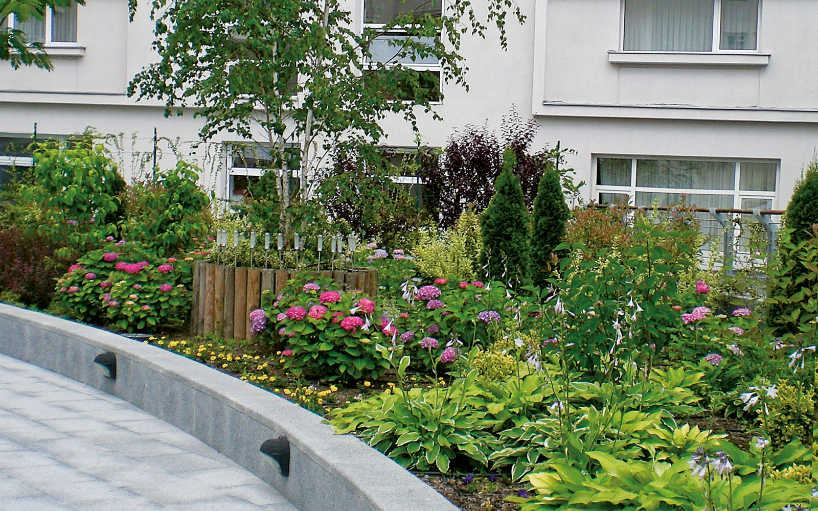 Curved plant beds with various small plants, shrubs and trees are built along the walkways. Plant beds with a small tree, shrubs and perennials